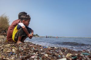 Dua anak sedang duduk di bibir Pantai Sendang Sikucing yang dipenuhi sampah